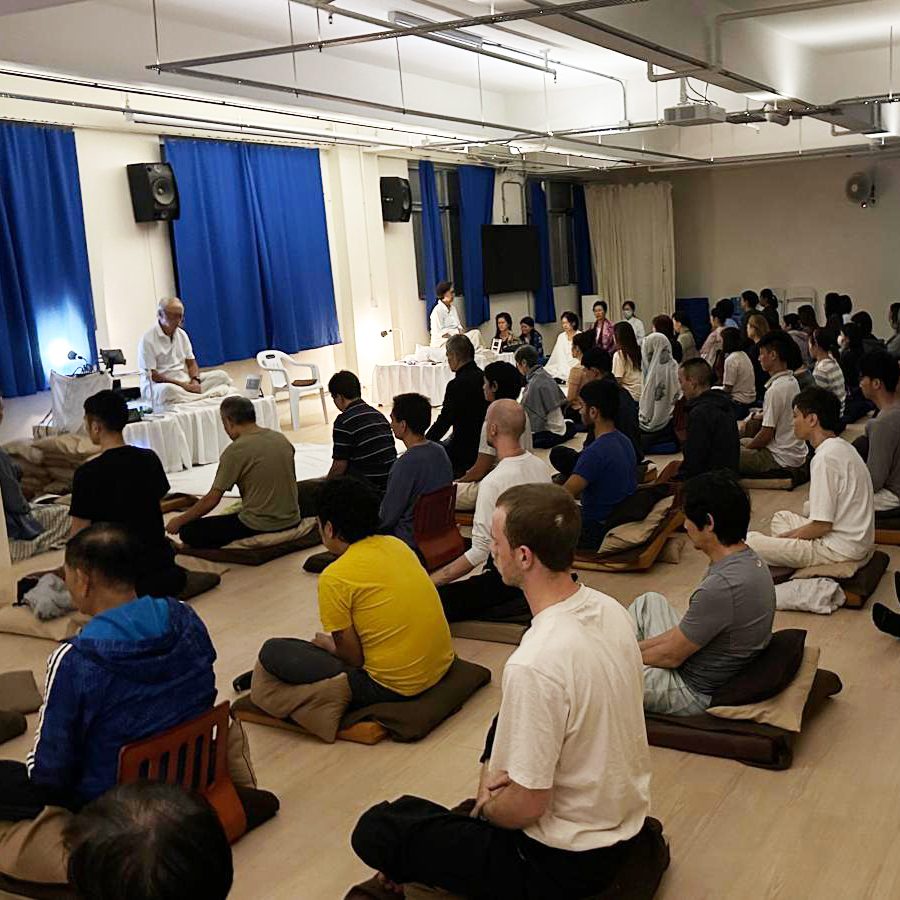 A large group of people sit cross-legged and meditate together during a vipassana course at Dhamma Mutta.